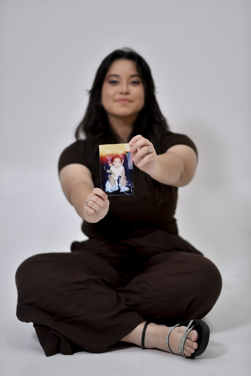 Gabi sentada no chão, segurando uma fotografia de bebê